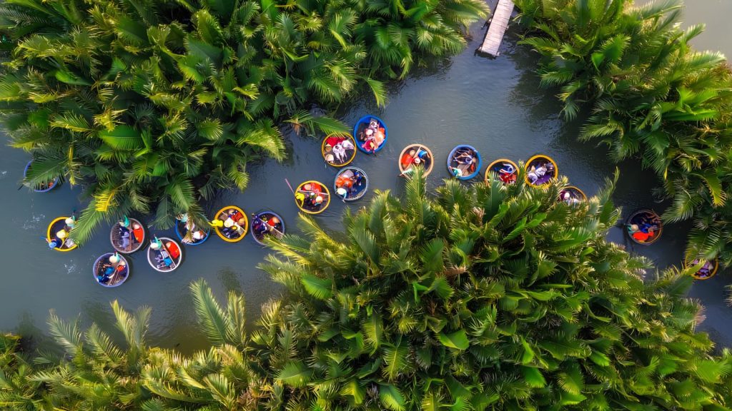 Colorful basket boats moving along a green canal through the coconut forest in Hoi An from above