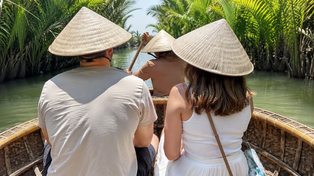 Tourists wearing conical hats sit inside a basket boat while exploring the peaceful canals of Cam Thanh Coconut Forest in Hoi An.