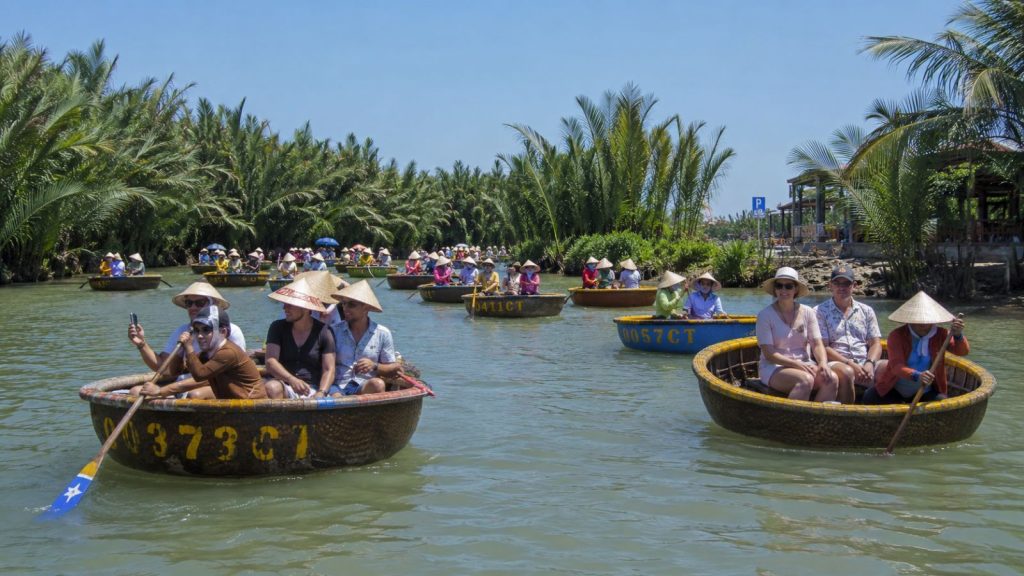 Multiple basket boats carrying tourists float along the river near Cam Thanh Coconut Forest, creating a vibrant Hoi An boat tour scene.