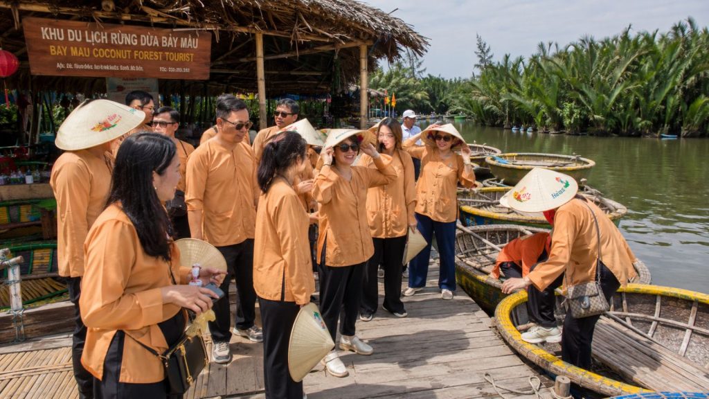 A company group wearing traditional outfits, scarves, and conical hats enjoys a basket boat tour through Cam Thanh Coconut Forest in Hoi An.