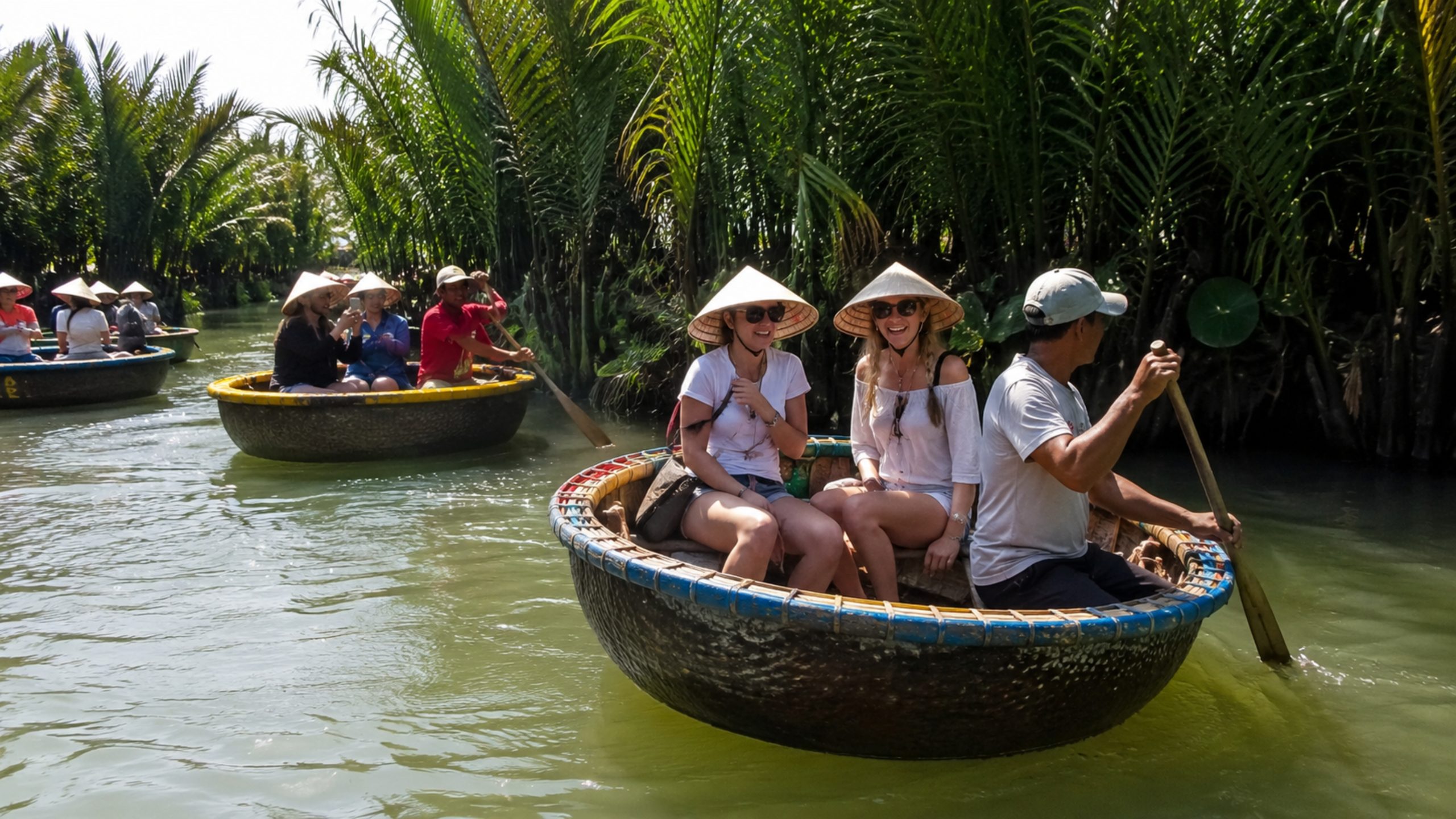 Foreign tourists wearing Vietnamese conical hats enjoying a basket boat ride in Hoi An Coconut Village.