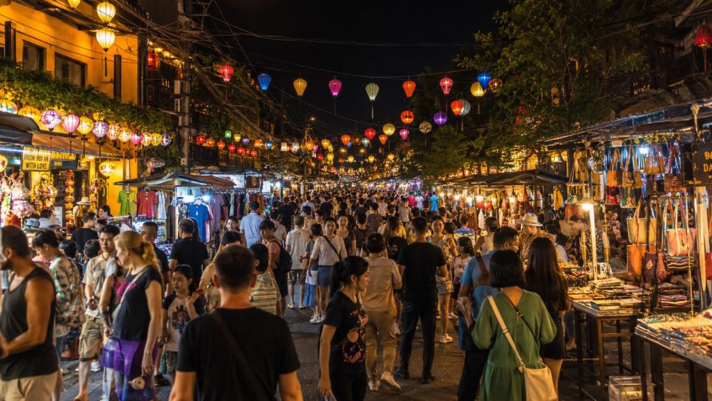 Hoi An Night Market is crowded with visitors browsing souvenir stalls under rows of colorful lanterns and warm street lights.