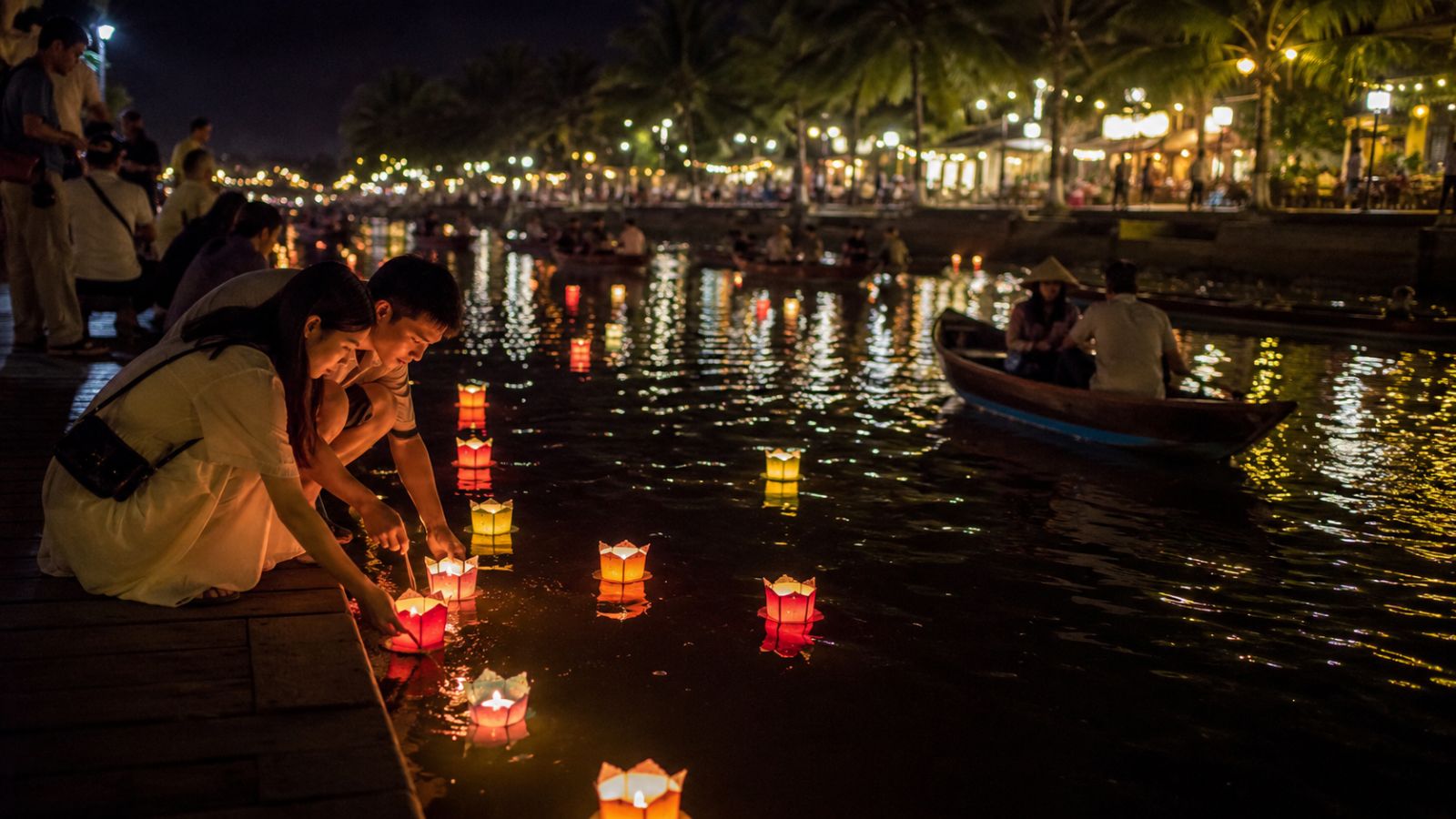 Hoi An Lantern Festival 2026 Dates, Schedule and Tips 2 Travelers releasing glowing paper flower lanterns onto the Hoai River from wooden boats in Hoi An