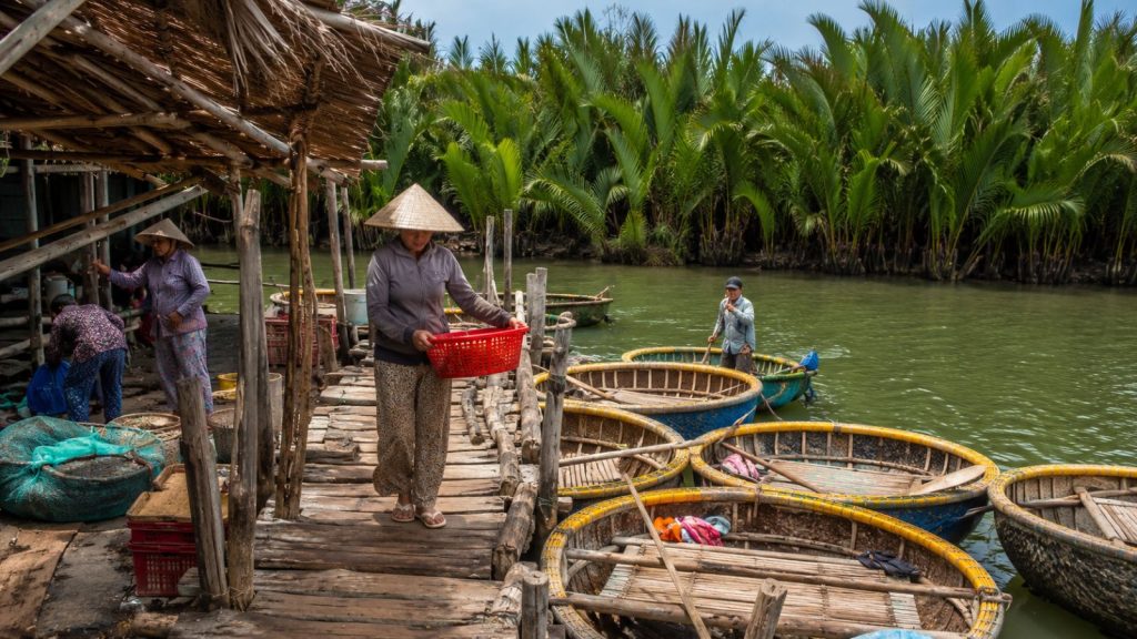 Traditional basket boats are docked beside a rustic wooden pier along the coconut-lined river in Cam Thanh Village.