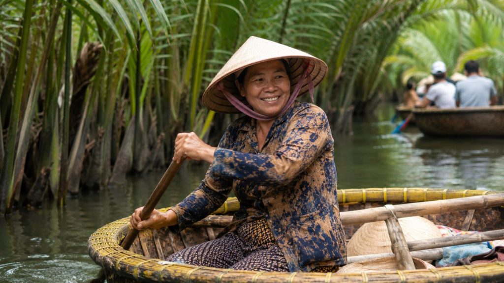 A smiling local woman rows a traditional basket boat through the narrow waterways of Cam Thanh Coconut Forest in Hoi An.