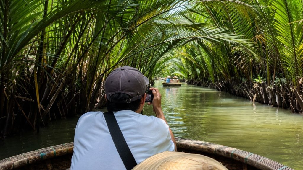 Best Cam Thanh Coconut Village Tour for a Unique Hoi An Experience 5 Traveler taking photos from a basket boat inside a lush coconut palm canal.