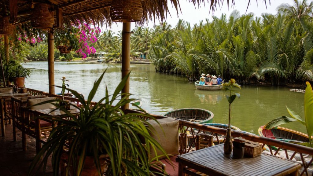 A quiet riverside café with basket boats and lush coconut palms creates a relaxing view in Cam Thanh, Hoi An.