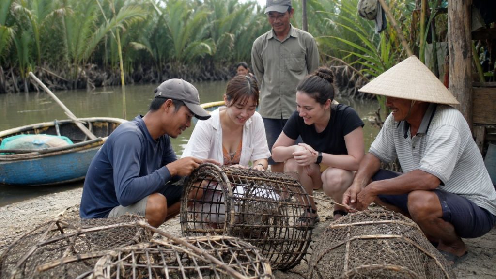 Local guides and travelers learn about traditional bamboo fishing traps beside the river in Cam Thanh Coconut Village.