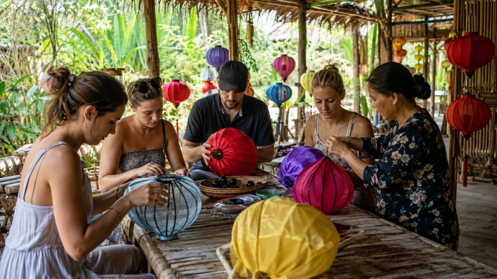 Visitors join a hands-on lantern making workshop with a local artisan in a rustic tropical setting near Cam Thanh.