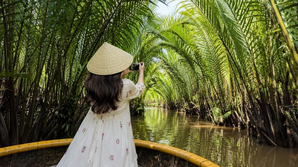 Tourist taking a photo in a basket boat inside a palm-lined canal.