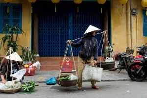 Tourist navigating crowded market vendors near Hoi An Ancient Town basket boat tour entrance with caution signs